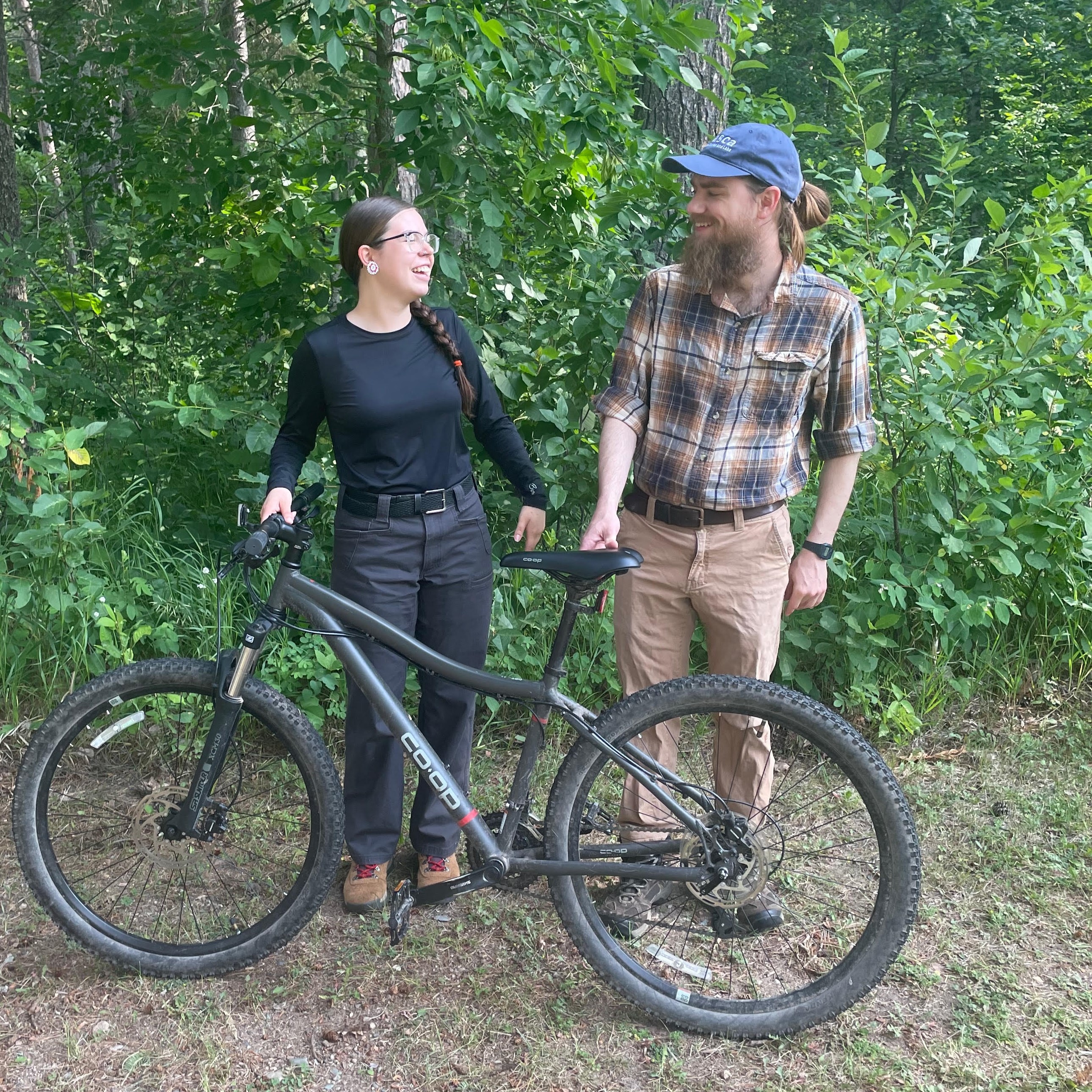 A woman in black holding up a bikeand man in plaid looking at each other and smiling.