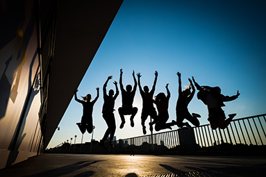 Outline of 7 students jumping excitedly with blue sky in background