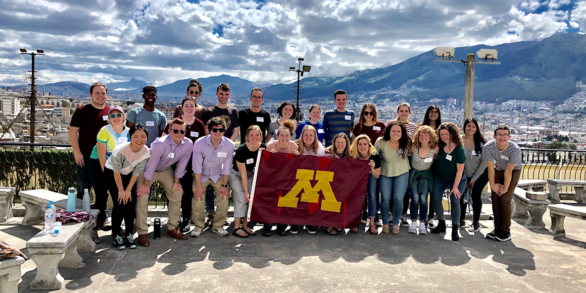 Group of students hold maroon M flag in front of mountains in Ecuador