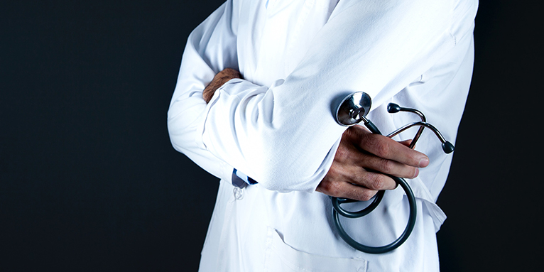 cropped image of person in lab coat holding a stethoscope with arms crossed at chest