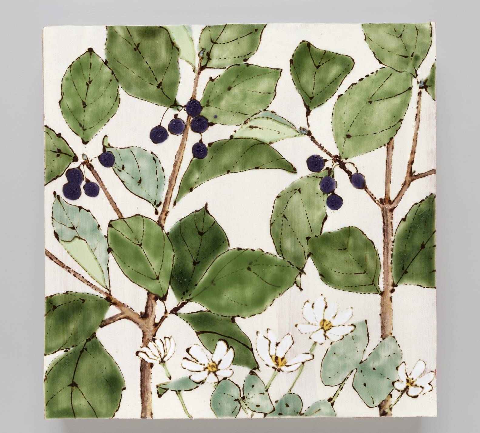 Photograph of a white ceramic tile painted with green buckthorn leaves and dark fruits.
