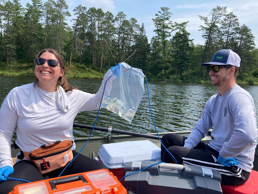 Two smiling researchers on a boat in Lake Deming, one holding a bag of collected samples