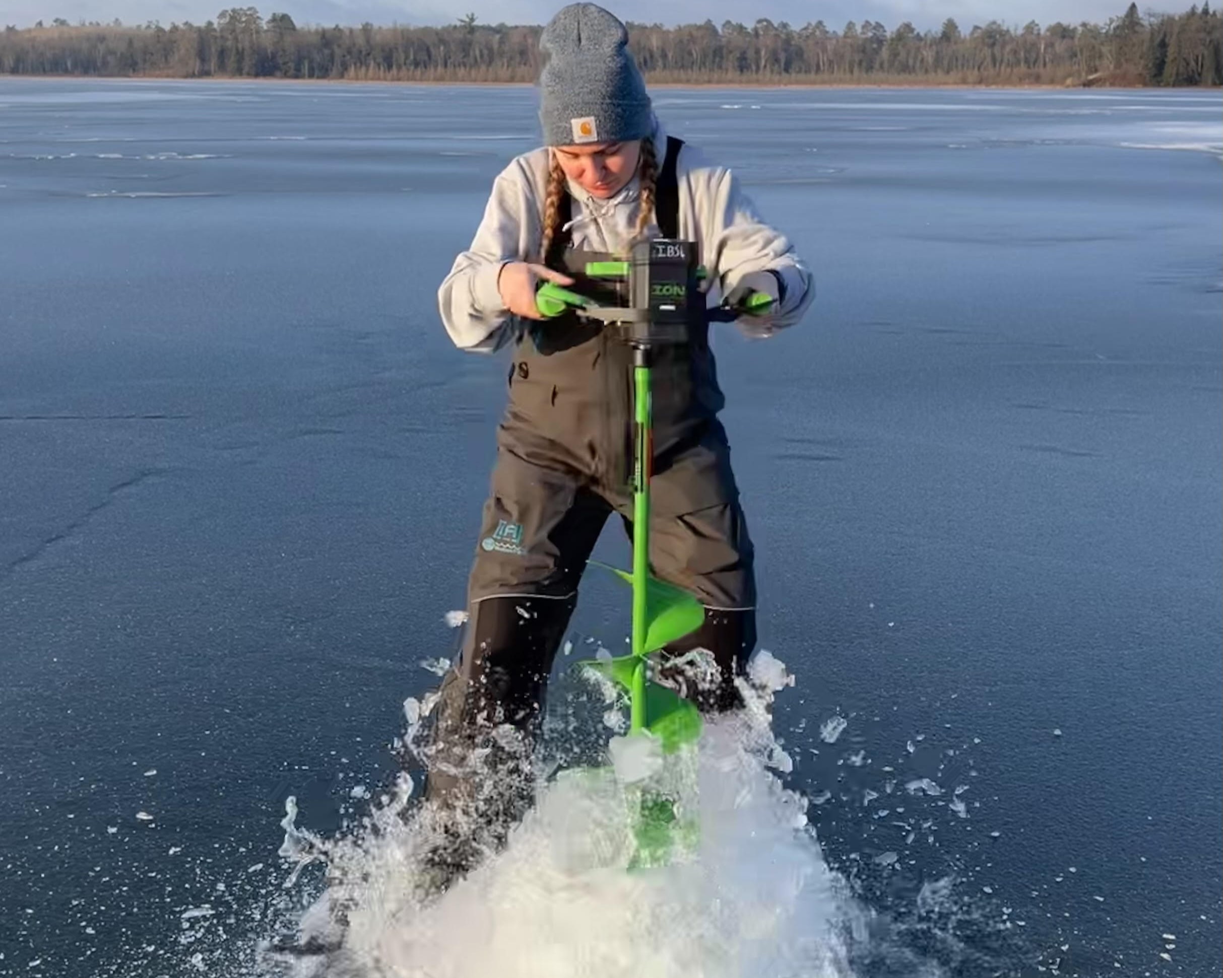 A woman with an ice auger drilling a hole in a frozen lake