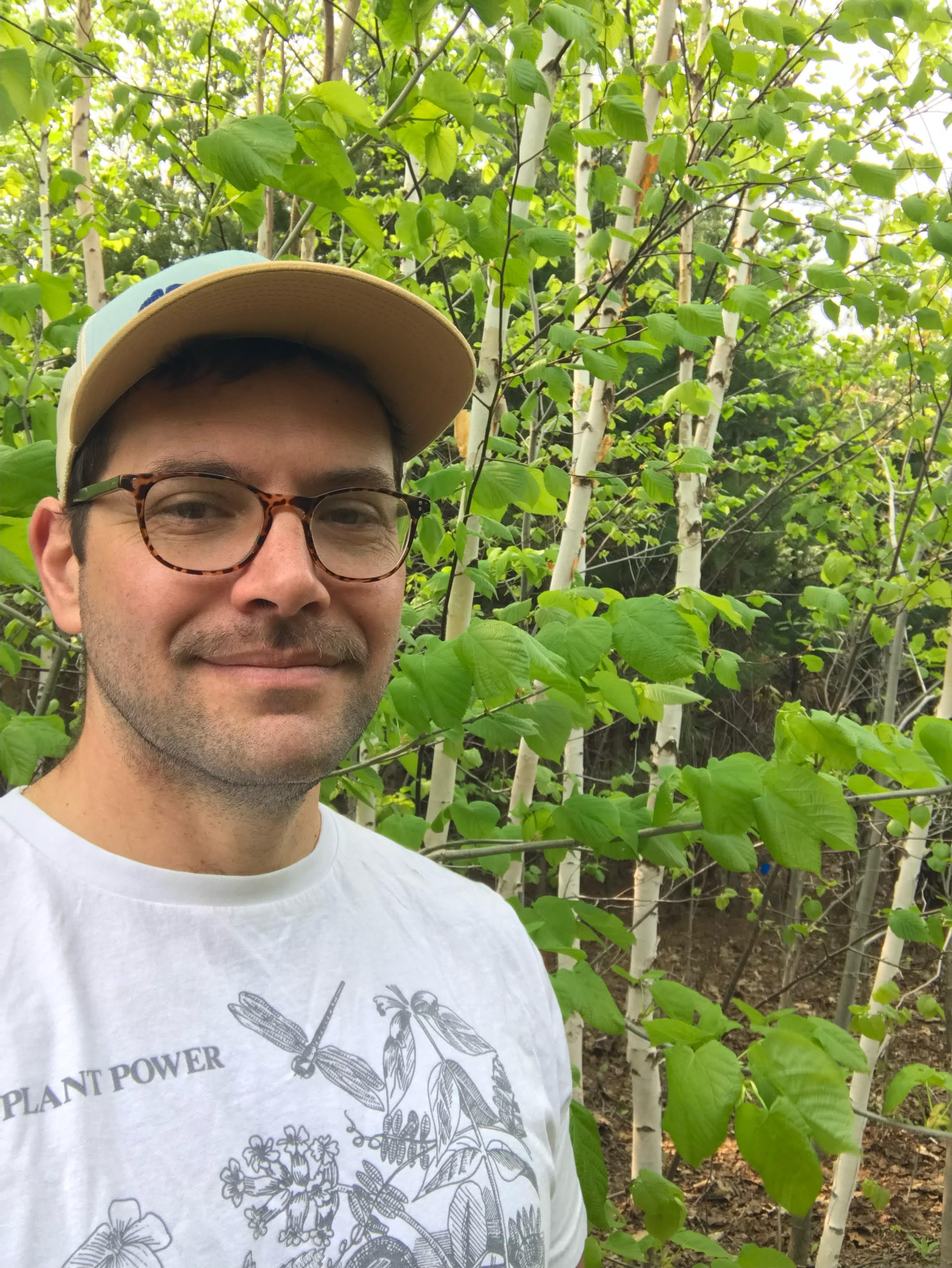 a man in glasses standing near trees