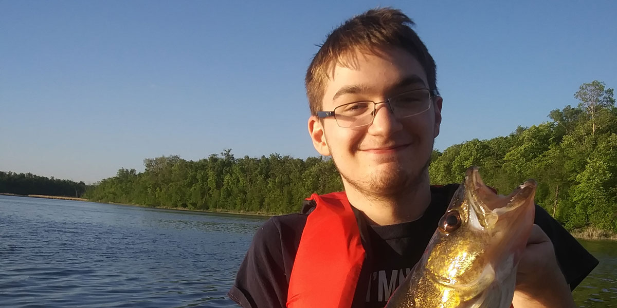 logan poses with a walleye wearing a red lifejacket and glasses
