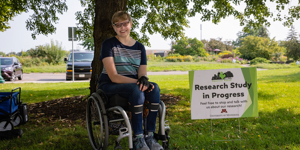Ph.D. student Charlotte Devitz next to a sign that reads "Research Study in Progress"