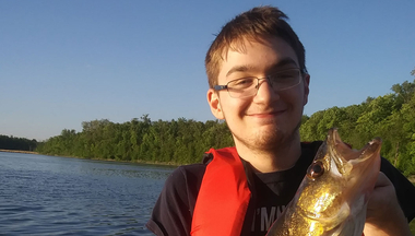 logan poses with a walleye wearing a red lifejacket and glasses