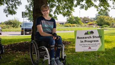 Ph.D. student Charlotte Devitz next to a sign that reads "Research Study in Progress"