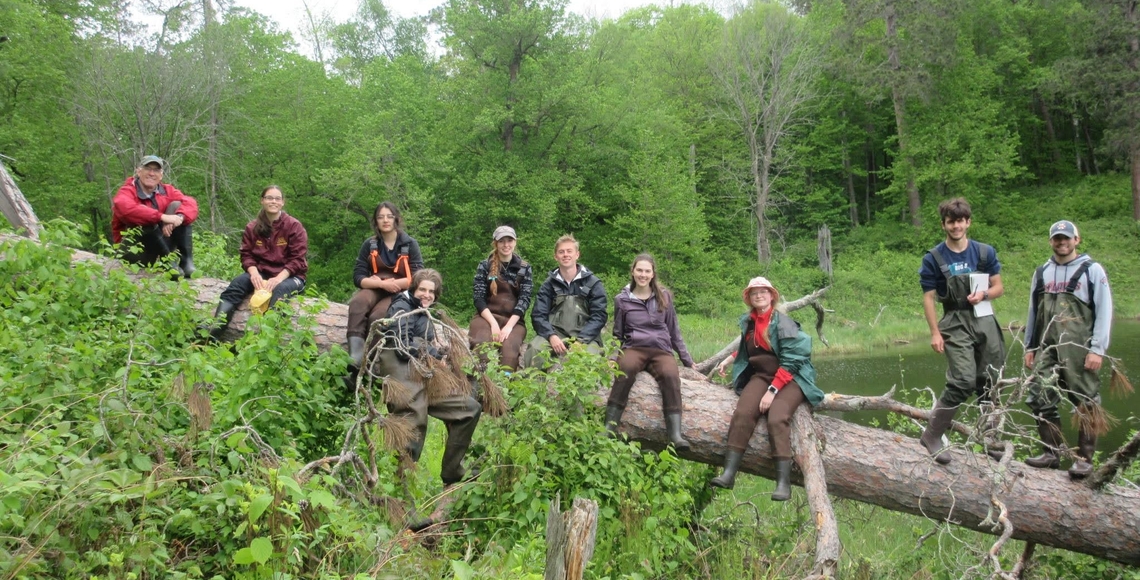 Instructor and students on a fallen tree in the woods