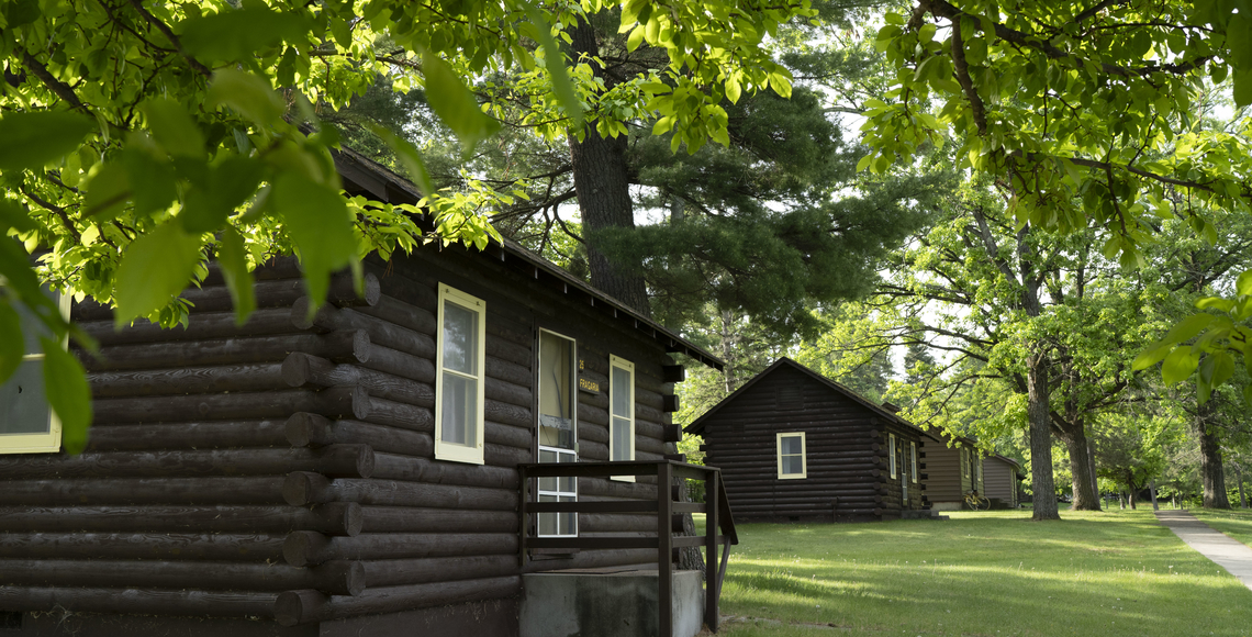 Front row of south-side student bunkhouse cabins at Itasca Station. Cabins shown are small, brown, log-style buildings.