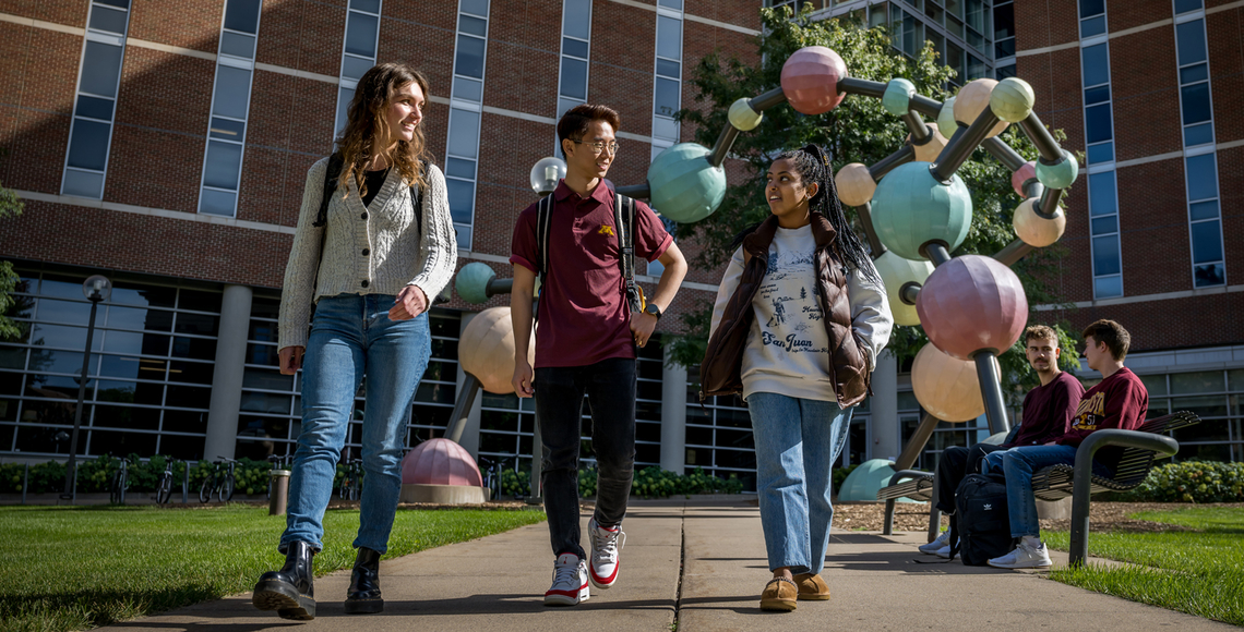 Students walking near MCB building on campus with the molecule behind them